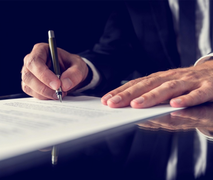 Close-up of a businessman in a suit signing a formal document with a pen on a reflective desk