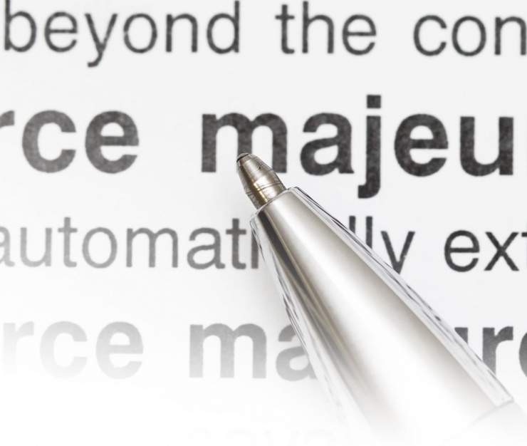 Close-up of a silver pen pointing to the words “force majeure” in a printed contract, highlighting legal implications of unforeseen events like COVID-19.