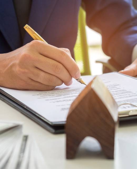 Close-up of a lawyer signing property transfer documents with house model and keys on the desk, representing conveyancing and notarial services at SWVG.