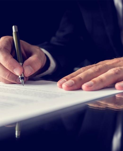 Close-up of a businessman in a suit signing a formal document with a pen on a reflective desk