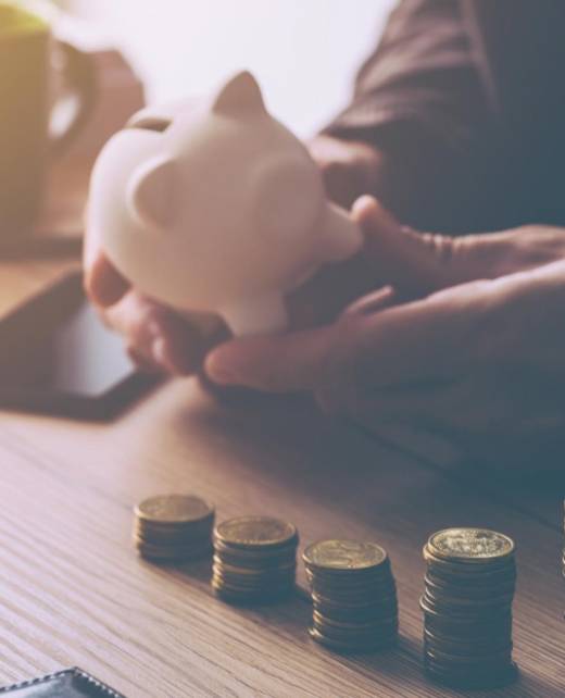 Close-up of a person holding a white piggy bank beside neatly stacked coins on a desk, symbolising financial recovery and debt collection services at SWVG.
