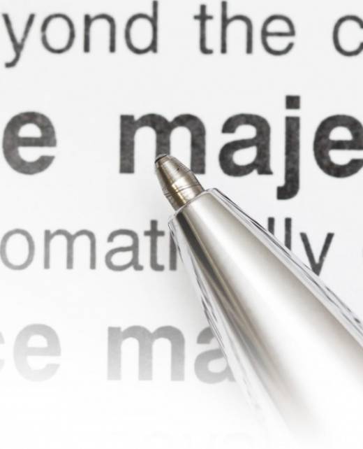Close-up of a silver pen pointing to the words “force majeure” in a printed contract, highlighting legal implications of unforeseen events like COVID-19.